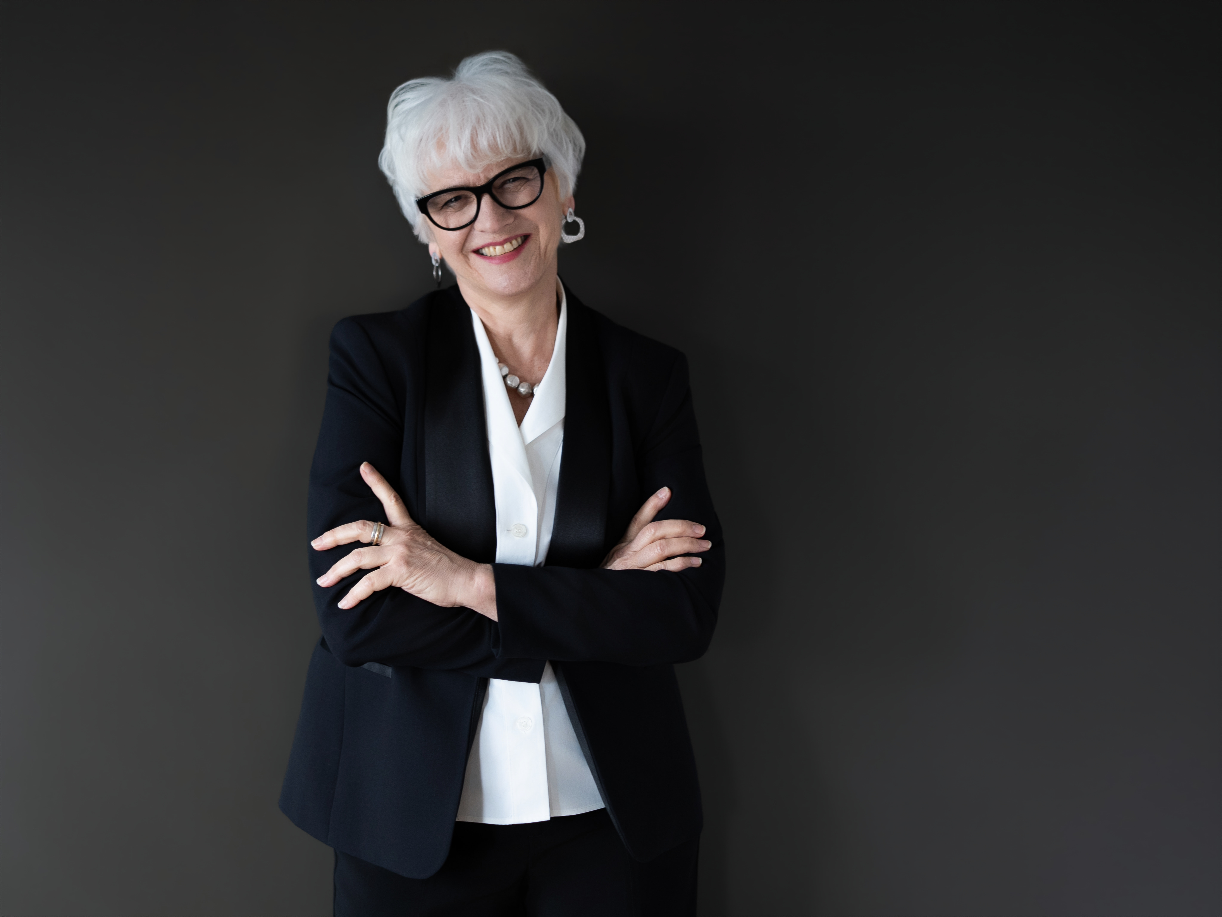 Portrait of Joan Szymko in a black blazer n front of a grey backdrop